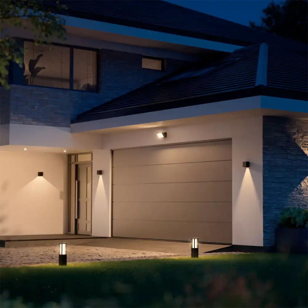 Aplique exterior Resonate Downward Philips Hue negro instalado en fachada moderna iluminando pared con luz blanca.