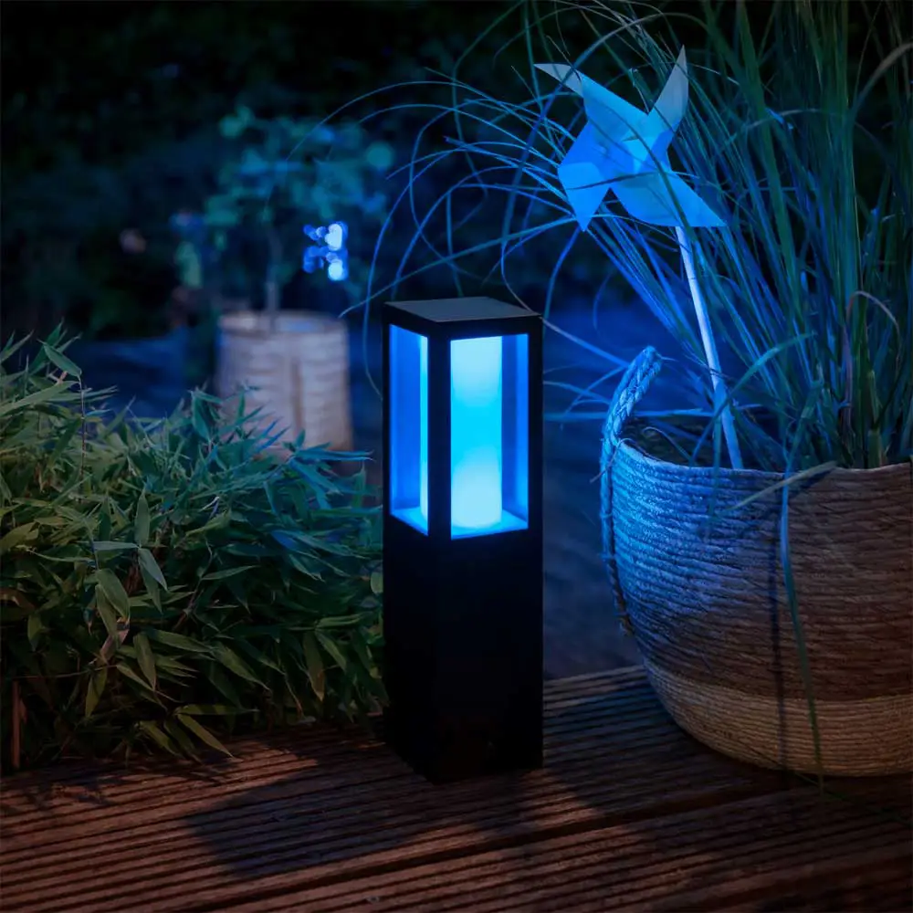 Baliza Impress Philips Hue negro instalada en exterior iluminando jardín con luz RGB azul y rosa.