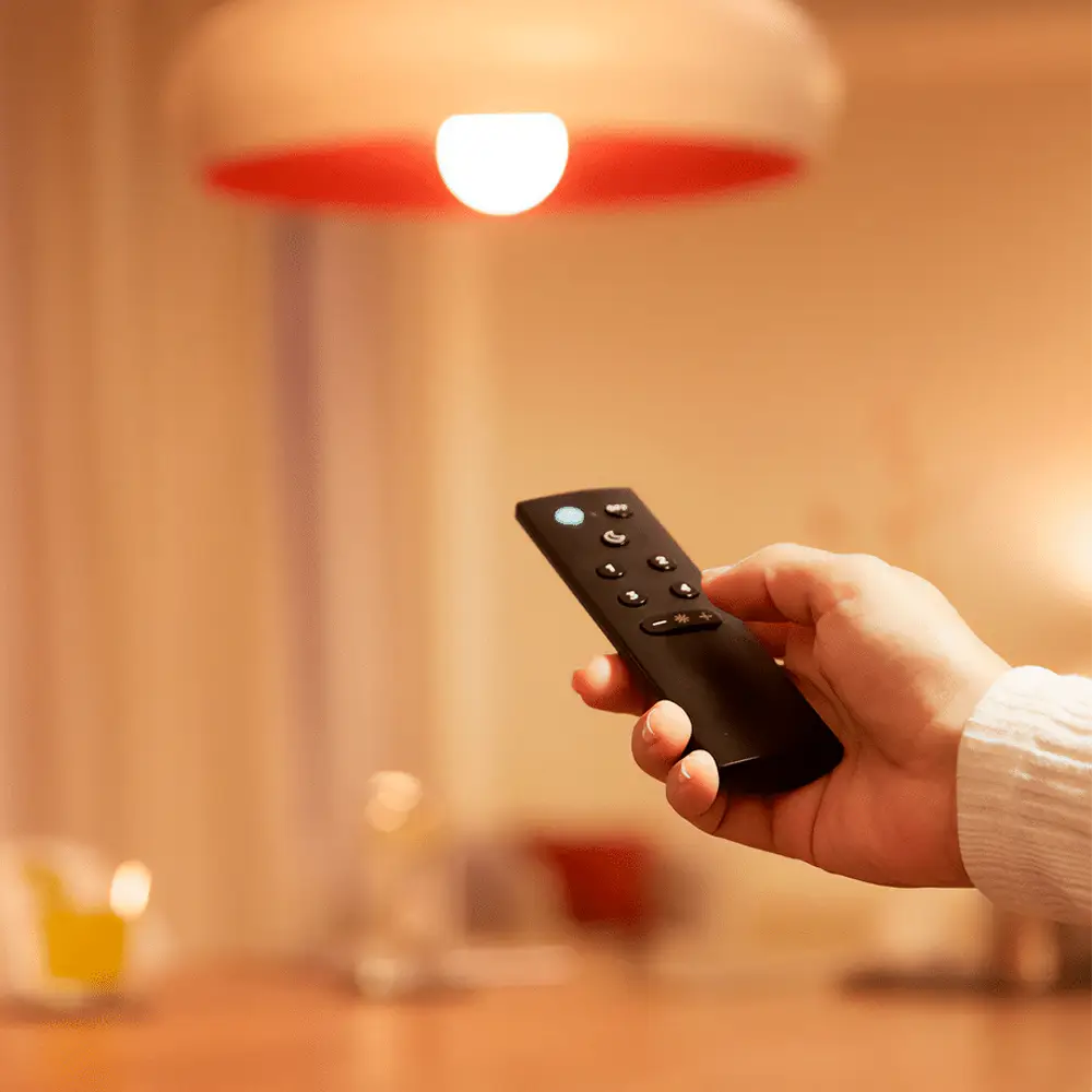 Persona utilizando control remoto para sistema WiZ Philips con lámpara encendida.